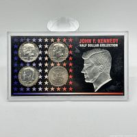 Front view of the plastic display case containing four John F. Kennedy half dollar coins with star pattern and Kennedy profile embossed.