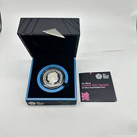 Silver proof £5 coin in black and blue display box with Royal Mint booklet alongside