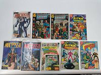 Top view of 10 comic books arranged in two rows. Titles include Macross II, Justice League of America, Batman Family, Aquaman, and Planet Comics. Covers show colorful superhero illustrations.