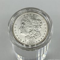 Top view of the 1887 Morgan Dollar coin in a transparent protective casing showing Lady Liberty profile and year 1887.