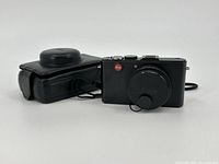 Front-left angle showing camera body, lens cap on and leather case beside.