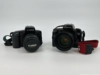 Front view of two Canon EOS film cameras, EOS Elan on left and EOS A2E on right each with lenses and straps attached.