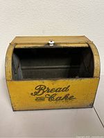 Front view of vintage yellow metal bread and cake box with sliding door open, showing interior and decorative typography