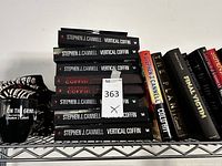Stack of multiple copies of Vertical Coffin paperback with partial view of other books