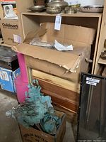 Cardboard box containing chafing dishes on cedar chest, metal garden decor stakes in 7-Up crate