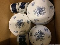 Eight large and six medium white bone china plates decorated with blue floral sprays, three cups at top left