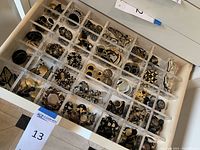 Top-down view of multiple clear-compartment tray showing gold and black earrings in each cell