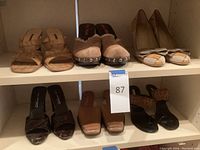 Shelf view showing seven pairs of ladies shoes displayed including woven heeled sandals, Miu Miu fuzzy mules, geometric pattern pumps with bow, snake print heeled sandals, tan low heels, and black flat sandals with cuff