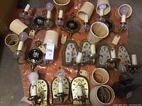 Overview of all sconces laid out on orange tarp: black disc and floral backplate fixtures, shades, drip sleeves