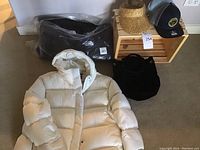 Overview showing both puffer coats, hats on wooden crate, and black velvet bag
