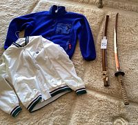Blue Patagonia fleece jacket and white Wimbledon jacket with green and purple striped cuffs and waistband, laid on beige carpet