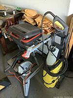 View of workbench with circular saw, stacked gloves, power washer with cord, and workbench details.