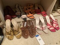 Overview of nine pairs of ladies designer shoes of various styles and colors arranged on floor and shelf