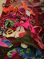 Assortment of ladies small swimwear pieces and colorful plastic sarong belt buckles laid out on a red fabric surface, showing various patterns and styles.