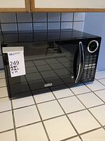 Front view of black Sunbeam microwave with keypad and digital display, showing overall condition and dimensions label.