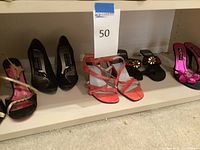 Full view of five pairs of women's shoes including high heels and sandals placed on shelf with visible straps, colors and styles.