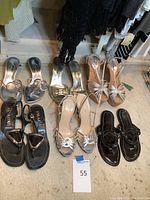 Full overview showing six pairs of women's designer shoes laid on floor – high heels and sandals in various metallic and black colors.