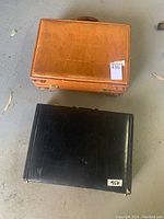 Two closed briefcases side by side on floor, black and tan brown exteriors
