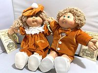 Two Cabbage Patch Kids Twin dolls seated next to each other with birth certificates and tags visible.