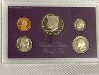 Five proof coins encased in clear plastic with purple background, showing coin faces including Lincoln penny, Jefferson nickel, Roosevelt dime, Washington quarter, and Kennedy half dollar.