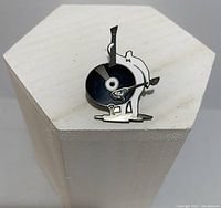 Front view of the ACME Studios pin showing the bass with record turntable body and bow shaped like a record player arm, displayed on a white pedestal.
