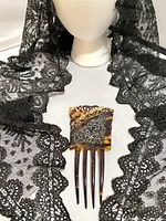 Decorative tortoiseshell-style hair comb placed on the mantilla fabric, showing silver-tone filigree detailing and prongs.