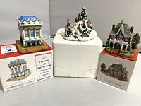 Photo of three boxed miniature buildings and one winter snowy hill scene figurine on a white background