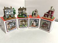Four Liberty Falls Village miniature buildings displayed on their original boxes, showing front views and packaging