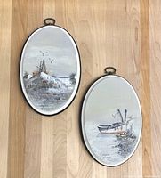 Pair of two hand painted oval paintings showing beach and boat scenes on a wood floor