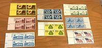 Top side of nine blocks of four uncancelled U.S. postage stamps in various designs including flags, planes, buildings, and symbols.