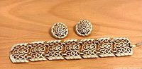 Gold tone filigree bracelet and clip-on earrings laid on wood surface from front view showing detailed scrollwork pattern.