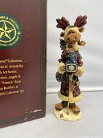 Front view of Montague Von Hindenmoose figure showing detailed moose Santa holding the jack-in-the-box and part of original box with Folkstone Collection branding.