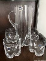 Clear crystal glass pitcher with handle and spout, surrounded by 4 matching tumblers. All pieces have Bohemia Crystal labels.