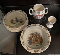Four pieces of Bunnykins fine bone china dishware: two decorated bowls, one handled mug, and one egg cup, each with colorful Bunnykins themed illustrations.