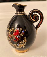 Black mini jug with butterfly and floral gold details on both sides and a curled handle with gold detailing