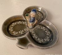 Top angled view of shamrock-shaped porcelain jewellery dish showing central figurine and shamrock pattern details.