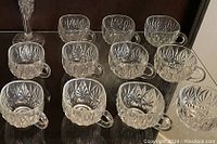Set of 11 clear crystal punch bowl glasses with diamond-cut pattern and handles, displayed grouped together.