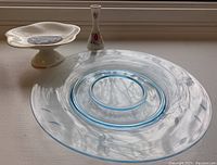 White pedestal serving plate with floral decoration and gold rim, along with small decorative vase