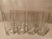 Front view of all 8 tall glasses arranged in two rows, showing the etched sailboat design and gold rim at the top of each glass.