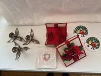 Photo showing the 3 metal candlesticks with holly and berries design, the handmade napkin basket and matching napkin rings, vintage disposable Christmas napkins in partially open package, and 2 vinyl coasters with skating reindeer design.