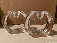 Front view of two clear round crystal taper candle holders showing their polished edges and sockets for candles.