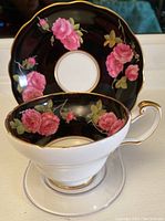 Photo showing teacup sitting on a clear stand in front of the matching saucer, highlighting floral design and gold trim