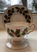 Teacup on display stand with holly and berry pattern, gold trim visible on rim and handle