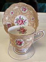 Photo showing teacup in front of matching saucer highlighting floral design and gold trim