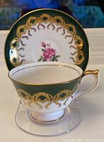 Photo of teacup with dark green background, gold scrollwork and pink rose floral design