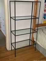 Full view of the 1980s shelving unit with four glass shelves and black iron frame.