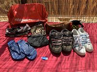 Overview of all footwear and vintage bags laid out on red surface under sunlight.