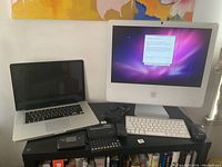 Photo showing Apple iMac desktop, MacBook laptop, iPad mini, keyboard, mouse, calculator, and cords on a black table