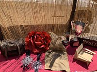 Overall view of most items on red cloth including gloves, rose prop, burlap sack, trophies, and small chair