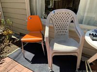Two chairs side by side: one orange indoor chair with chrome legs and one beige plastic patio chair with armrests and lattice backrest.